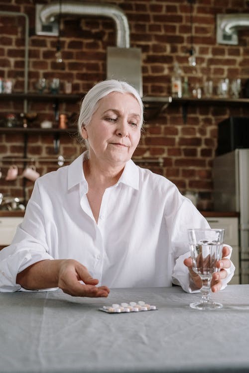 An elderly woman takes her medication which is placed on the table.