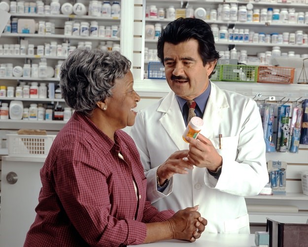 An elderly woman talks to her pharmacist regarding her prescription.