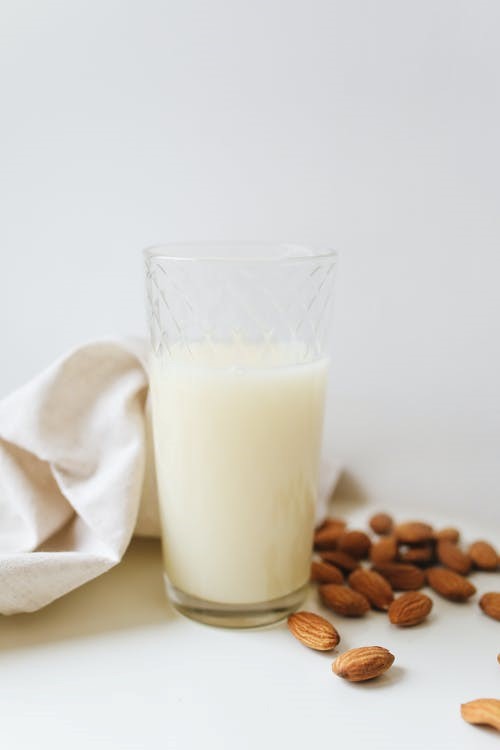 A glass of milk placed next to almonds