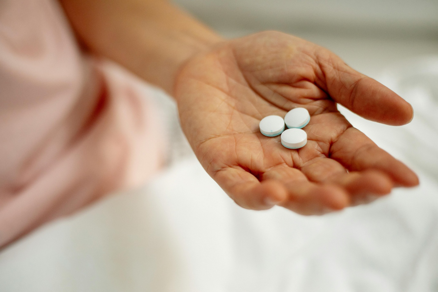 a person holding three white pills in their hand