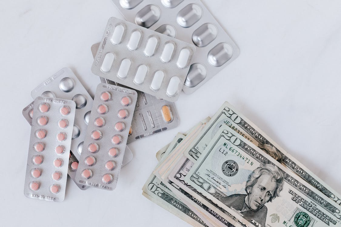 The image shows a collection of pill blister packs alongside several U.S. dollar bills.