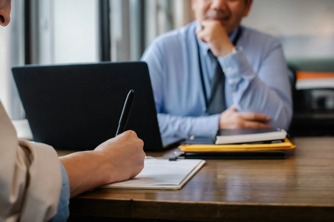 A man signing paperwork opposite another man at a desk