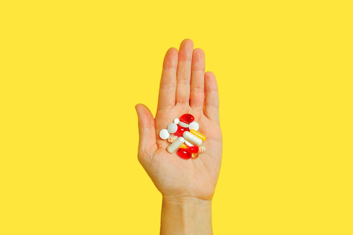 A hand holding some medicines against a yellow background