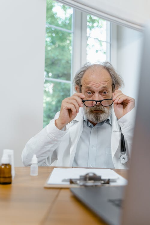 Older doctor adjusting glasses while reviewing information at a desk